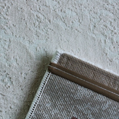 Tapete tecido bege com borda castanha sobre tapete felpudo claro com padrão