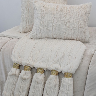 Conjunto de almofadas e manta creme com franjas e strass dourado sobre cama clara