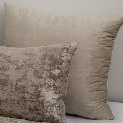 Duas almofadas decorativas bege com tecidos diferentes sobre superfície branca
