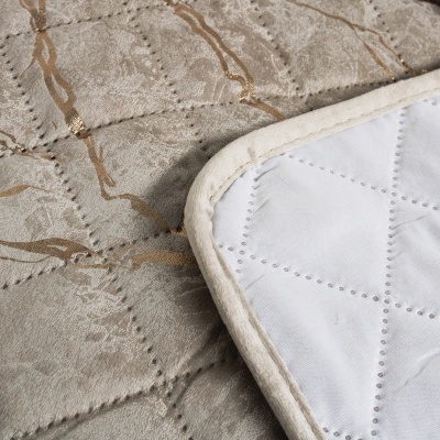 Colchão cinzento com padrão dourado e tapete branco bordado no canto