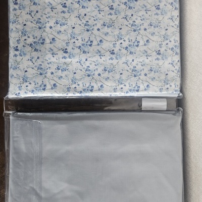 Conjunto de roupa de cama com padrão floral azul e lençol azul claro embalados em plástico.