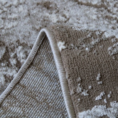 Tapete castanho com padrão abstrato branco e bege, canto dobrado mostrando lado inferior