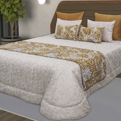 Conjunto de cama com edredão bege, manta e almofadas decorativas castanhas e cinza, com planta ao fundo