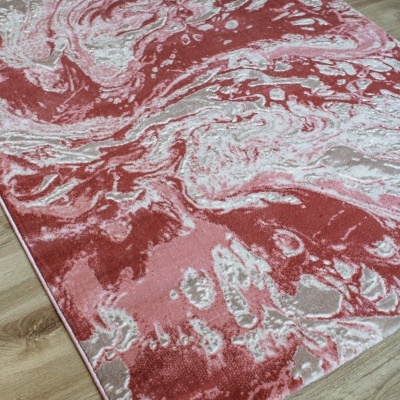 Tapete decorativo abstrato em tons vermelhos e rosa sobre chão de madeira