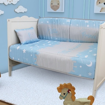 Cama infantil branca com roupa de cama azul clara estampada com estrelas e texto Little Prince