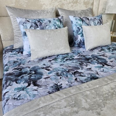 Cama com colcha e almofadas decorativas em padrão floral azul e veludo cinza