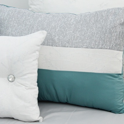 Duas almofadas decorativas, uma cinza, branca e azul-esverdeada, outra branca com botão prateado