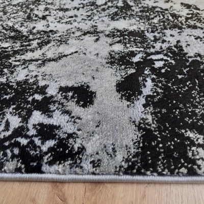 Tapete cinzento e preto com padrão abstracto sobre chão de madeira