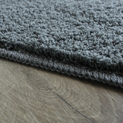 Tapete cinzento felpudo com borda costurada sobre chão de madeira clara