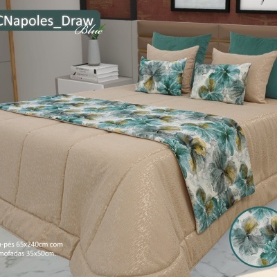 Cama com colcha bege e almofadas florais em tons verde, cinza e amarelo num quarto com mesa de cabeceira branca, livros e vaso.