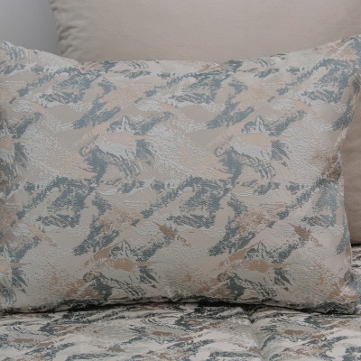 Almofada com padrão abstrato em tons de bege e azul sobre cama