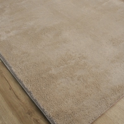 Tapete bege claro felpudo sobre chão de madeira clara.
