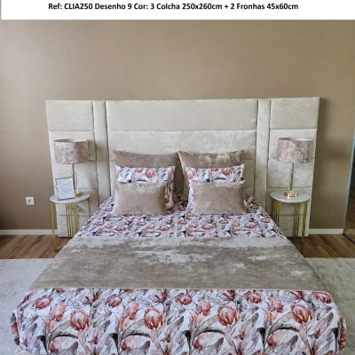 Cama com colcha floral cor de rosa e bege com cabeceira estofada e duas mesas laterais com abajures.