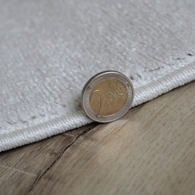 Tapete branco macio com moeda de 2 euros na borda sobre chão de madeira clara