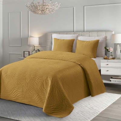 Cama com colcha e almofadas mostarda com padrão ondulado em quarto decorado com mobília branca e iluminação suave