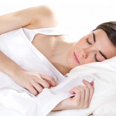 Mulher a dormir numa cama com roupa de cama branca