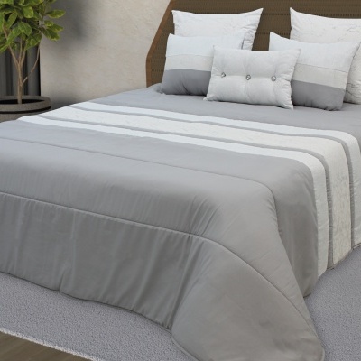 Cama com colcha cinza e almofadas brancas e cinzentas, tapete cinza e planta verde ao lado