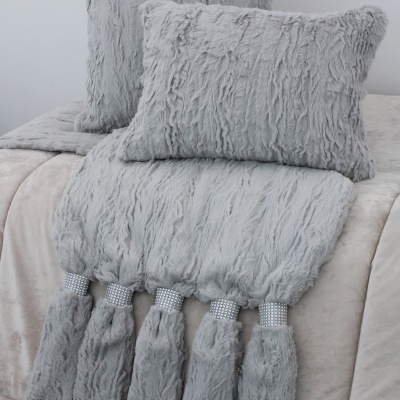Conjunto de almofadas e manta cinzentas felpudas com franjas brilhantes sobre cama clara