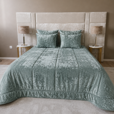 Cama com cabeceira estofada bege, edredão e almofadas verde-água, mesas de cabeceira douradas com candeeiros.