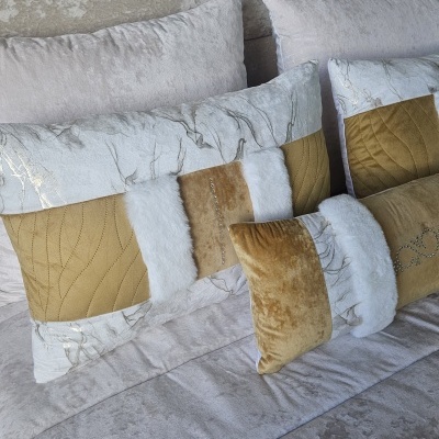 Três almofadas decorativas em tons bege, branco e dourado sobre sofá cinzento