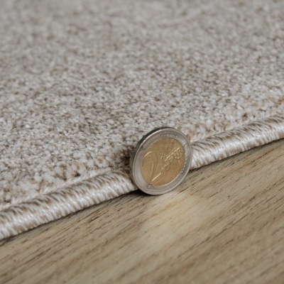 Tapete bege claro com textura felpuda e borda resistente sobre chão de madeira clara e moeda de 2 euros à frente