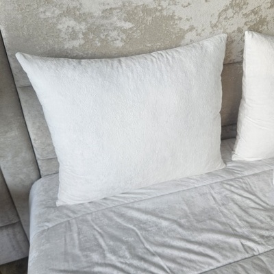 Travesseiro branco sobre cama com lençol branco e cabeceira estofada cinza