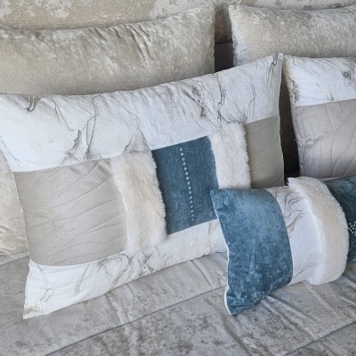 Almofadas decorativas em tecido bege, azul e branco com texturas variadas sobre sofá cinzento
