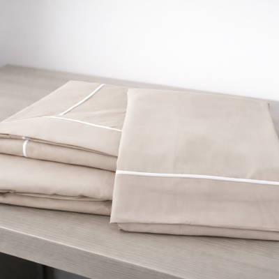 Conjunto de lençóis bege com costura branca dobrados numa mesa de madeira clara