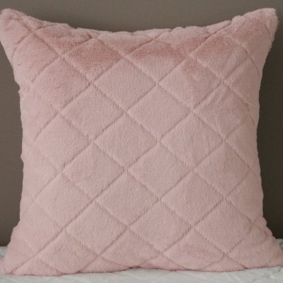 Almofada rosa com padrão em relevo sobre superfície branca e parede cinza
