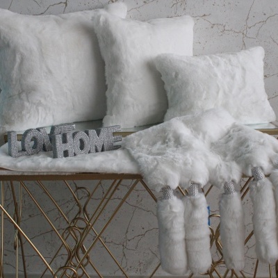 Almofadas e manta brancas felpudas sobre banco dourado com texto decorativo HOME