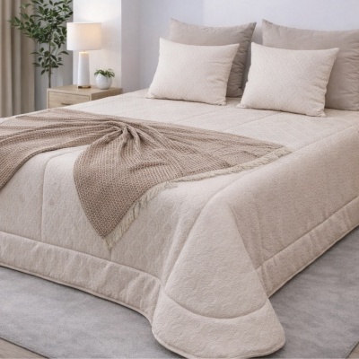 Cama com edredão bege claro, almofadas e manta de tricô bege escuro numa decoração minimalista.