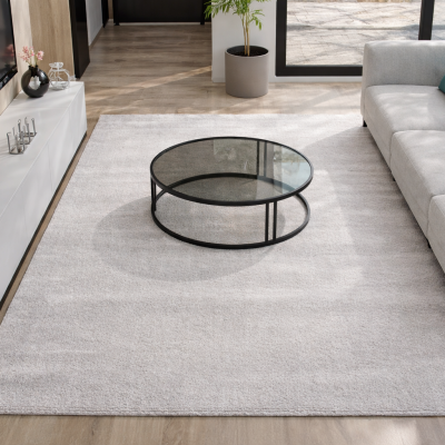 Sala de estar moderna com sofá cinza claro, mesa de centro redonda de vidro, tapete branco e móvel branco