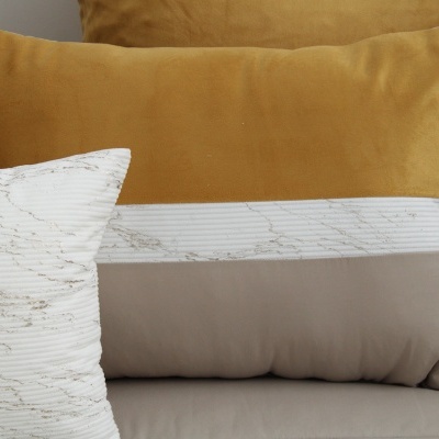 Almofadas amarelo-mostarda e retangular branco, cinza com padrão abstrato em sofá.