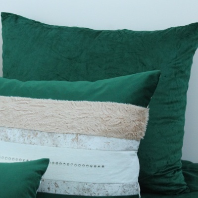 Três almofadas verdes com detalhes bege e prateados num sofá ou cama verde.