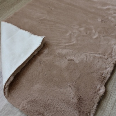 Tapete castanho felpudo sobre chão de madeira clara com um canto dobrado