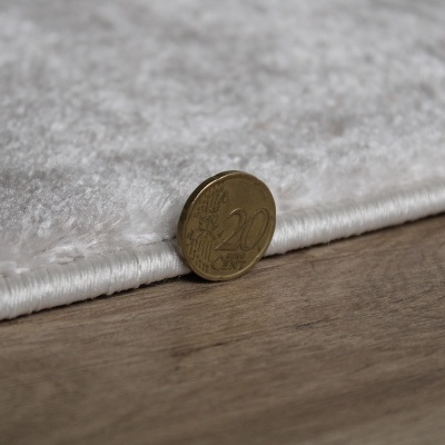 Moeda de 20 cêntimos ao lado de tapete branco em chão de madeira