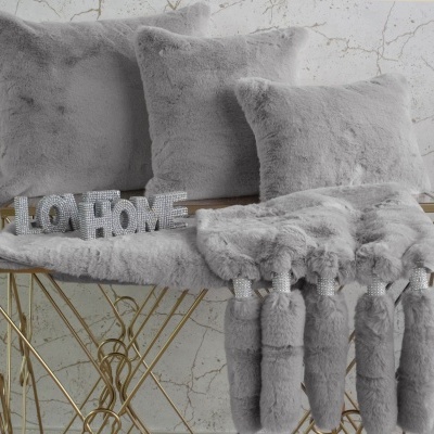 Almofadas e cobertor cinza felpudo com letreiro LO HOME em superfície metálica dourada