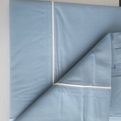 Roupas de cama azul claro com linha branca dobradas em superfície clara