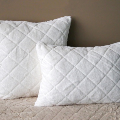 Duas almofadas brancas felpudas com padrão acolchoado sobre superfície bege e parede castanha.