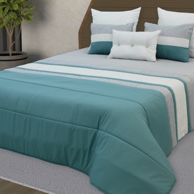 Cama com colcha azul turquesa e branca com faixa, almofadas coloridas, cabeceira em madeira e planta ao lado