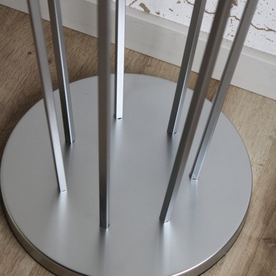 Base circular metálica prateada com seis hastes verticais em chão de madeira