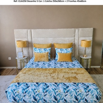 Cama com colcha floral azul e verde e almofadas amarelas, cabeceira estofada bege, mesas e candeeiros laterais amarelos.