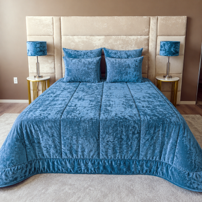 Cama com edredão azul e almofadas em quarto com cabeceira creme e mesas de cabeceira com lâmpadas azuis