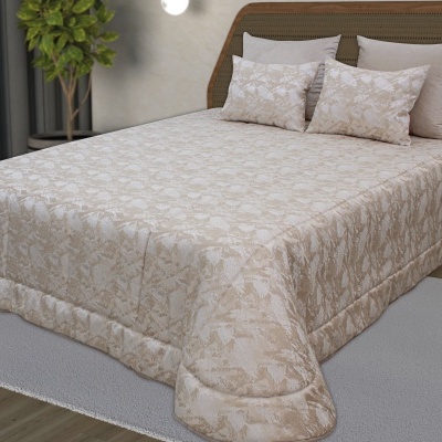 Conjunto de cama com edredão e almofadas bege com padrão floral, cabeceira de madeira e tapete cinza.