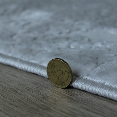 Moeda de 20 cêntimos ao lado de tapete cinzento claro sobre chão de madeira