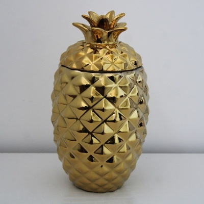 Recipiente dourado em forma de ananás com tampa decorativa.