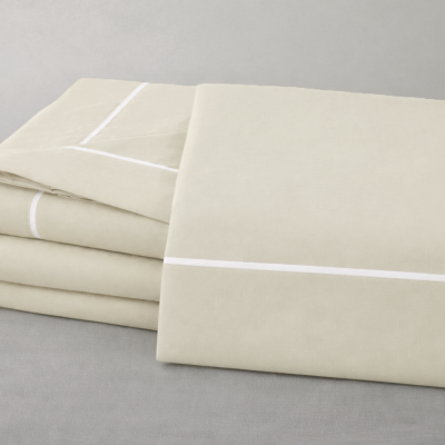 Conjunto de roupa de cama bege claro com linhas brancas finas dobrado sobre superfície cinzenta