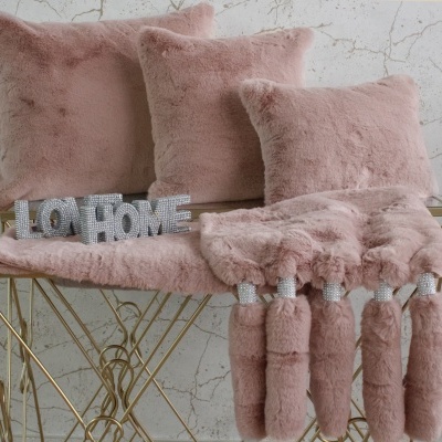 Almofadas e manta cor de rosa peludas sobre mesa metálica dourada com letras decorativas OHOME