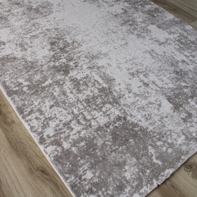 Tapete retangular cinzento claro e branco com padrão abstrato sobre chão de madeira.