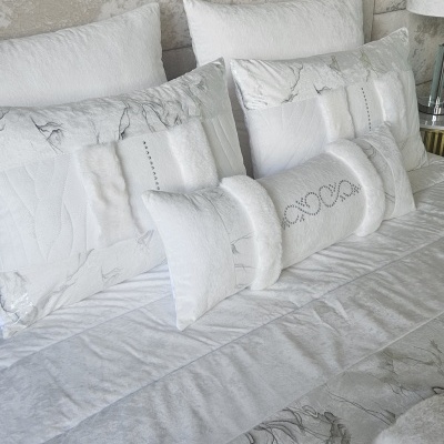 Conjunto de almofadas e edredão branco com padrão marmoreado e detalhe em pedrarias na almofada decorativa.